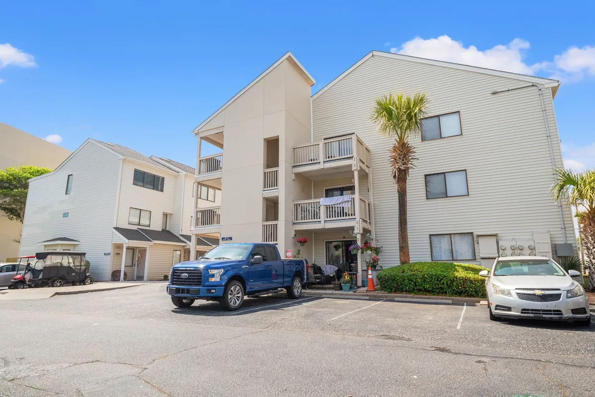 A welcoming exterior shot of the multi-story condo building, accented by palm trees and parked vehicles. Balconies suggest spaces for socializing outdoors, while the sunny weather adds to the inviting atmosphere.