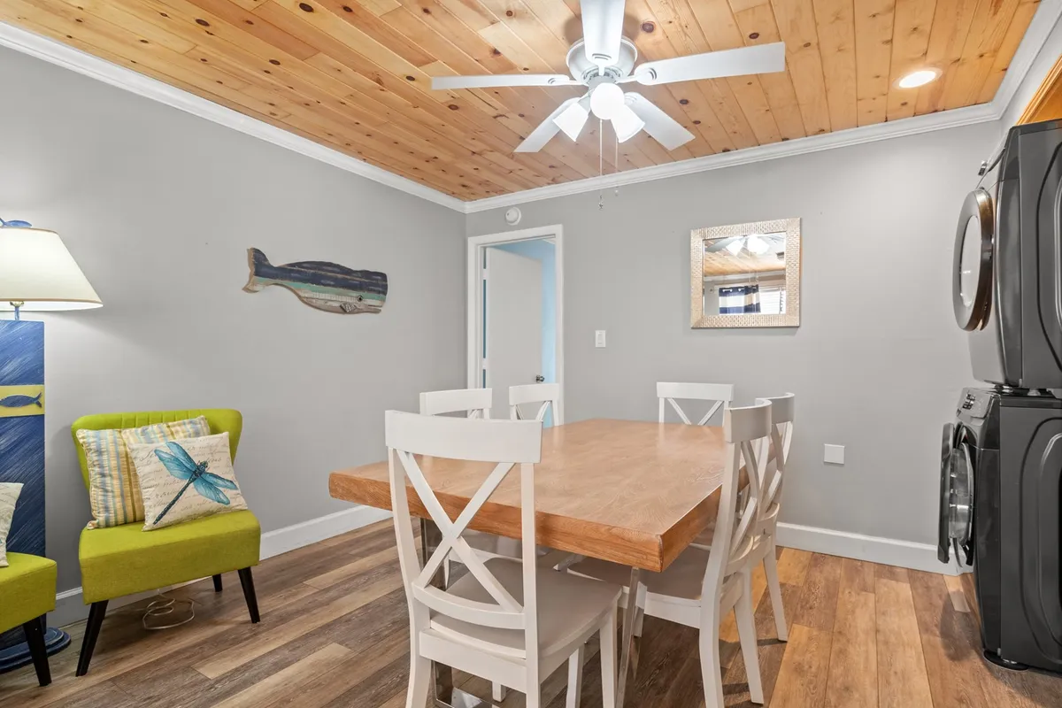A friendly, relaxed dining area is featured here, centered on a dining table with a distinctive green chair, wall artwork, and a ceiling fan overhead. The setting suggests shared family meals, game nights, and memorable gatherings.