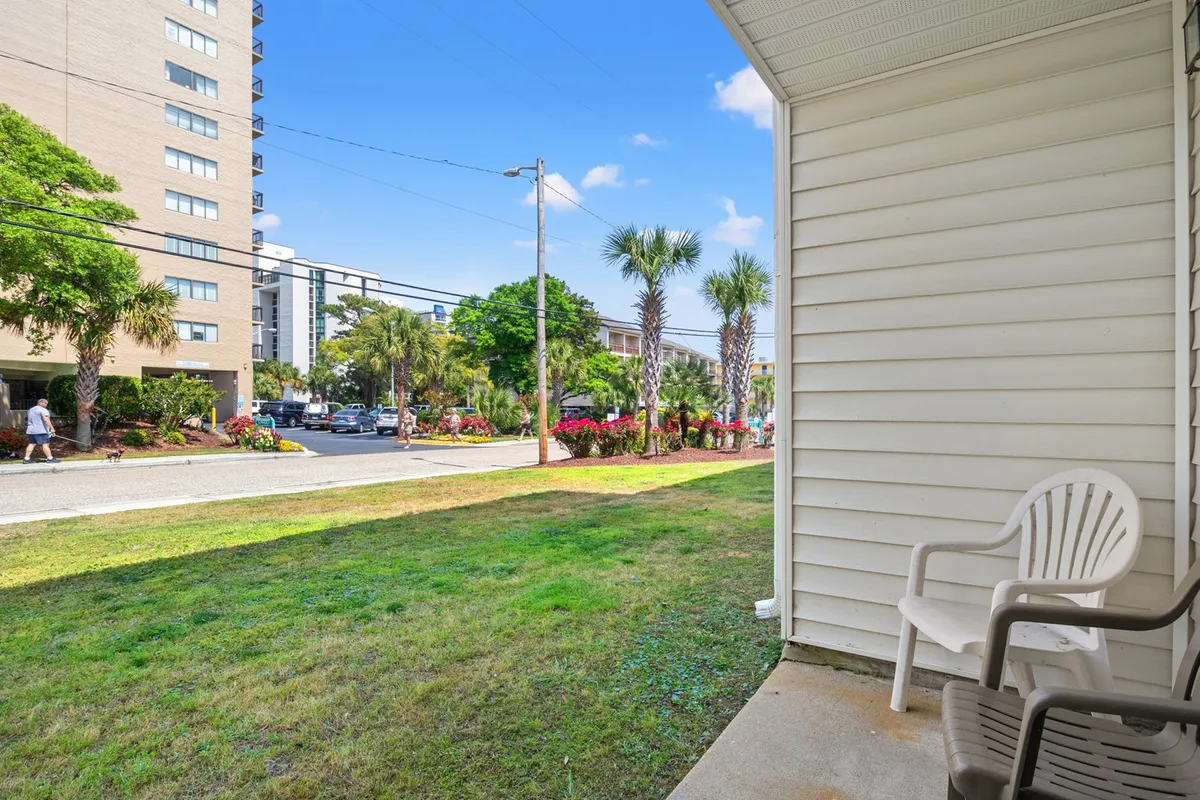 Palm trees and blooming flower beds line a sidewalk in front of the building, with a cheerful facade. The scene suggests a friendly neighborhood atmosphere and easy access to outdoor spaces, ideal for enjoying fresh air with minimal effort.