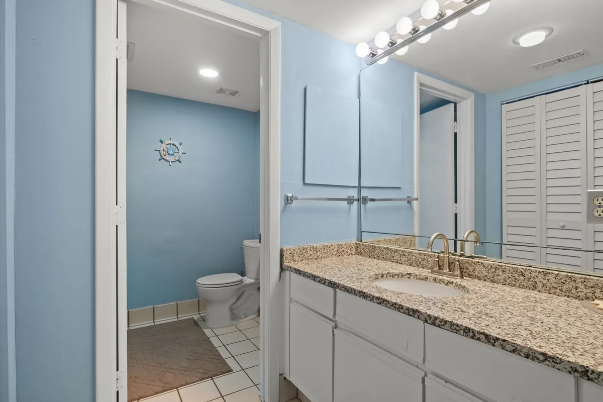 A calm and inviting bathroom space with a granite countertop, mirror, and toilet. The neutral tones and clean design create an ideal setting for relaxation and self-care.