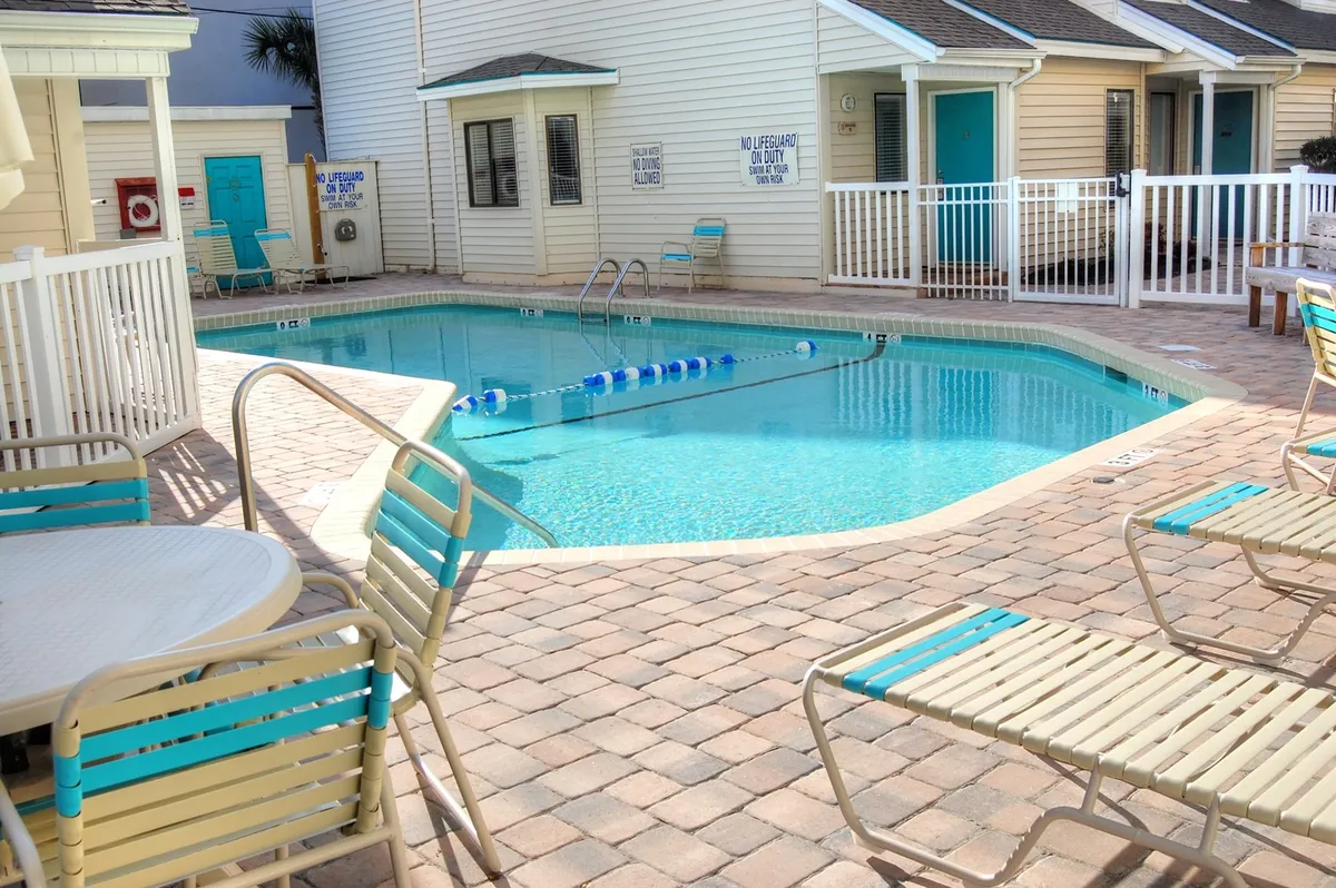 An inviting exterior view of a sparkling swimming pool surrounded by lounge chairs and cozy cottages. The scene is sunlit and welcoming, perfect for a relaxing afternoon after a busy day of exploration.