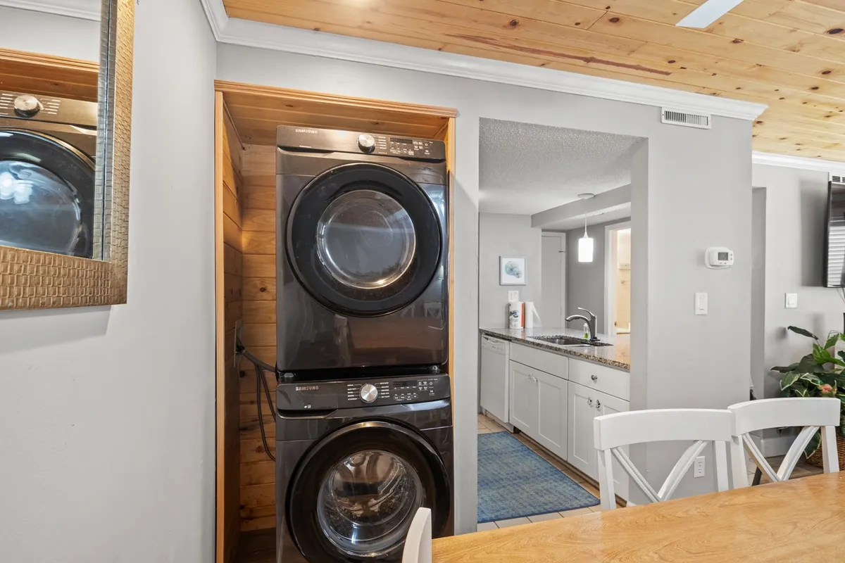 This image shows a stacked washer and dryer tucked conveniently into a nook near a dining table, with a cozy wooden ceiling above. The space is neat and accessible, highlighting the functional yet welcoming aspect of the villa's layout.