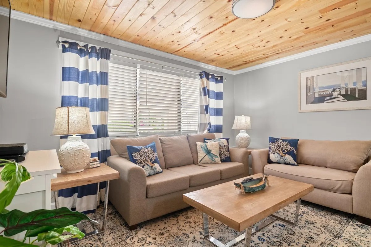 This image highlights a cozy interior living room featuring plush sofas adorned with decorative cushions, a coffee table, and light curtains. The space exudes warmth and comfort, perfectly suited for conversation, relaxation, and quiet reading sessions.