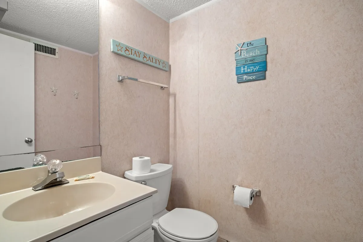 A tranquil bathroom featuring a sink, toilet, and charming beach-themed decorative signs. The space feels fresh and relaxing, ideal for personal grooming and unwinding after a long day.